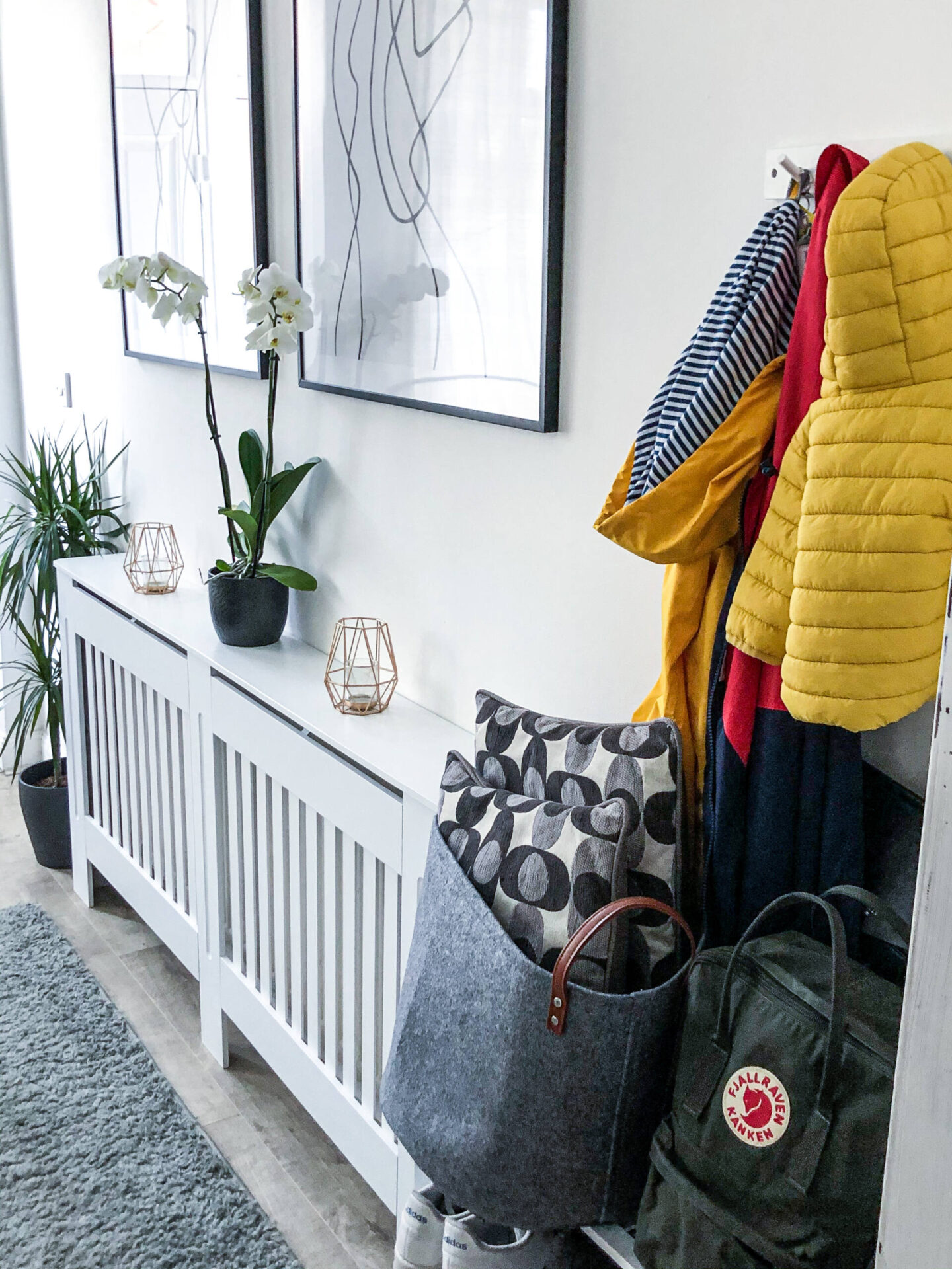 Desenio line art posters above a radiator cover and yellow jackets 